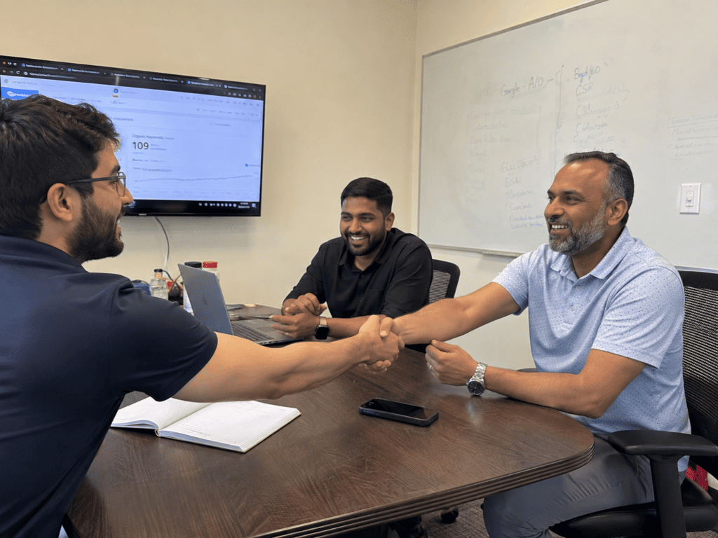 Three men at a conference table shaking hands, indicating a formal agreement or collaboration in a corporate environment.