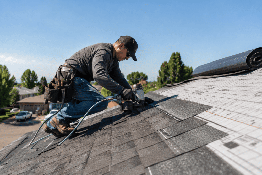 A man using a tool while working on a roof, focused on his task in a clear blue sky.