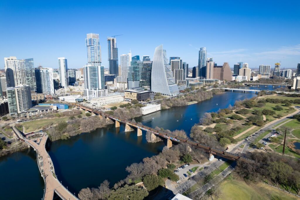 pexels-photo-18583622-18583622 Aerial view of Austin, Texas skyline with landmarks including river and footbridge.
